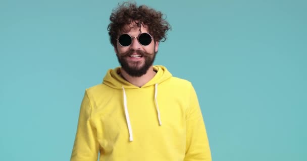 노란색 스웨트 셔츠를 섹시하고 턱수염의 복강경 선글라스를 스튜디오에서 파란색 배경에 — 비디오