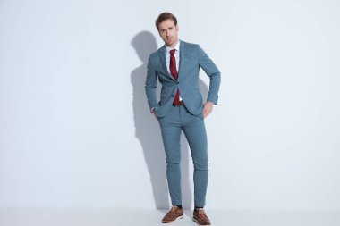 Zarif mavi takım elbiseli kendine güvenen sakallı adam stüdyoda gri arka planda poz verirken el ele tutuşuyor.