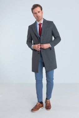 Çekici iş adamı ceketini kapatıyor ve moda pozuyla kameraya bakıyor.