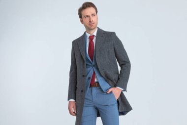 Zarif yakışıklı işadamı bir elini cebine sokuyor ve başka yere bakıyor.