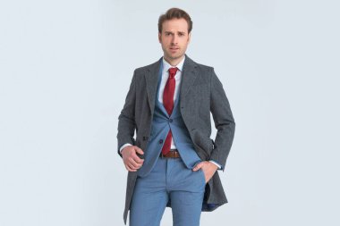 Seksi genç işadamı bir elini cebine sokuyor, ceketini tamir ediyor ve kameraya bakıyor. 