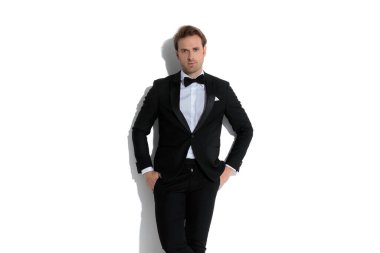 Seksi iş adamı ellerini ceplerine sokup duvara yaslanıyor.