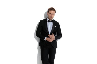 Genç yakışıklı iş adamı avuçlarını ovalıyor ve beyaz bir duvara karşı havalı poz veriyor.