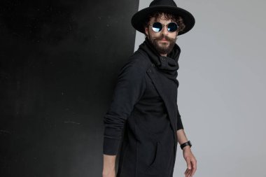 Uzun sakallı ve bıyıklı, eski moda güneş gözlüğü takan ve stüdyoda siyah ve gri arka planda poz veren seksi Latin adamın yan görüntüsü.