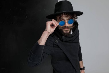 Siyah şapkalı çekici sakallı bir adamın portresi. Stüdyoda siyah ve gri arka plana bakıyor.