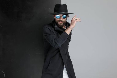 Stüdyoda siyah beyaz arka planda uzun sakallı, havalı bir genç adamın portresi var.