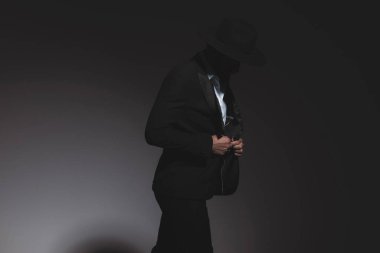 Gizemli manken ceketini ayarlıyor ve aşağıya bakıyor, gri arka planda dramatik oluyor.