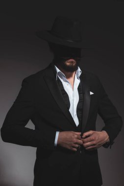 Siyah şapkalı ve papyonlu gizemli iş adamı smokinini gri arka planda kapatıyor.