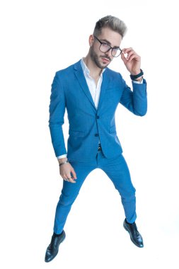 Takım elbiseli, kolsuz tişörtlü, gözlüklü ve moda pozunda duran çekici, zarif bir adam. Stüdyoda beyaz arka planda tüm vücuduyla poz veriyor.