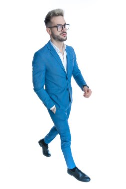 Tıraşsız, takım elbiseli ve gözlüklü çekici bir adamın yan görüntüsü. El ele tutuşup stüdyoda beyaz arka planda tek başına yürüyor.