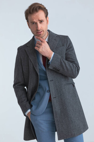 сексуальный бизнесмен чувственно трогает подбородок, смотрит в камеру и сует одну руку в карман