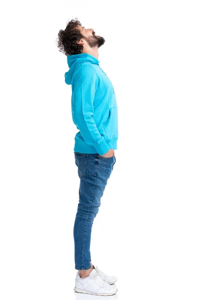 サイドビューの巻き毛の男で青いパーカーはポケットに手を取りながらスタジオで白い背景の上に立ち — ストック写真