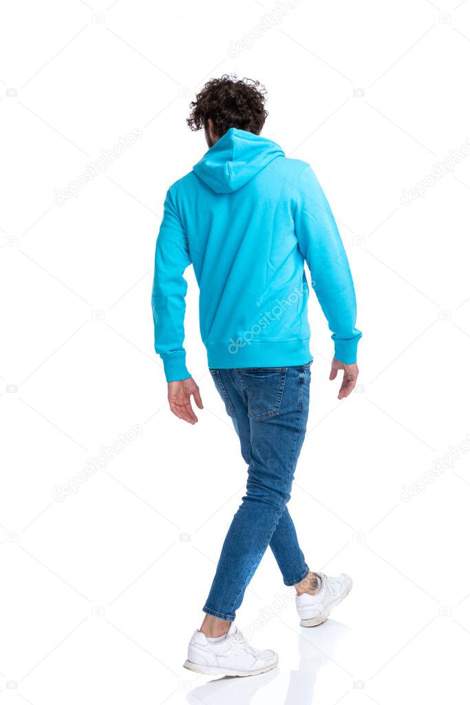 back view of casual model in hoodie looking to side and walking isolated on white background in studio, full body