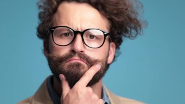 creative young fashion model rubbing chin and beard, thinking and having an idea, getting excited and proud on blue background in studio