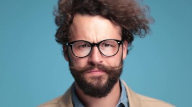 suspicious casual bearded man investigating, making serious faces, smiling and making ok gesture, approving on blue background in studio