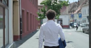 Kahveli ve bavullu çekici bir adamın arkadan görünüşü, yürüme ve dans etme, parmaklarını gösterme ve Romanya 'dan gelen bir ortaçağ şehrinde mutlu olma