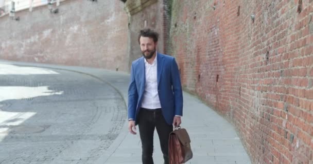 青いジャケットを着てスーツケースを持って自信を持ってルーマニアから中世の街を歩いているセクシーな剃毛のない男 — ストック動画