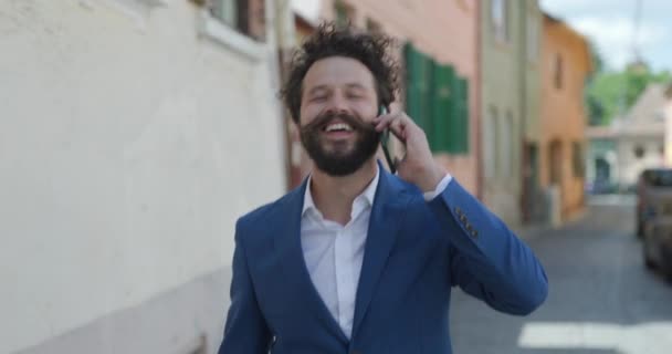 迷人的卷发男人走路 拿起电话 聊得很开心 在户外热烈交谈 — 图库视频影像