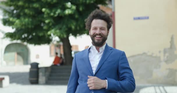 Jovem Atraente Com Cabelo Encaracolado Barba Ajustando Jaqueta Sorrindo Acenando — Vídeo de Stock