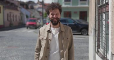 Genç, sıradan bir adam kameraya gülümseyip iki koluyla işaret ediyor ve dışarıda heyecanlanıyor.