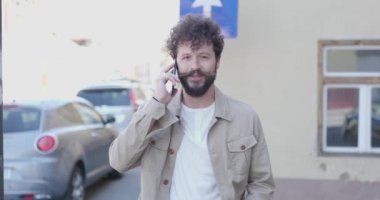 Seksi manken telefonda konuşuyor ve şehirde kameraya gülümsüyor.