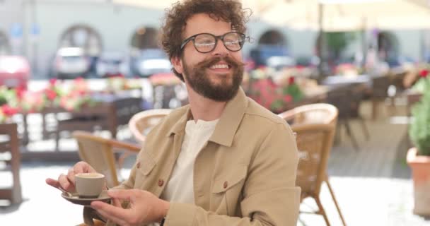 Siedzący Swobodny Mężczyzna Uśmiechający Się Kogoś Pijący Kawę Zadowolony Niej — Wideo stockowe