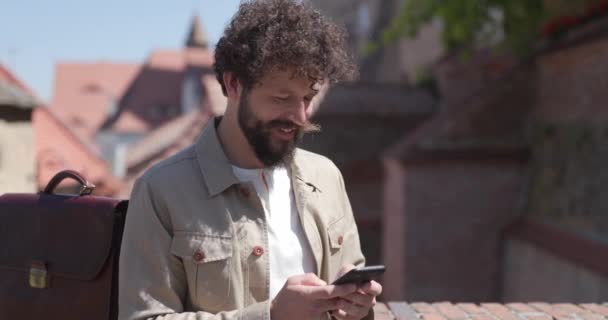 Jonge Casual Man Leunend Naast Zijn Aktetas Sms Aan Telefoon — Stockvideo