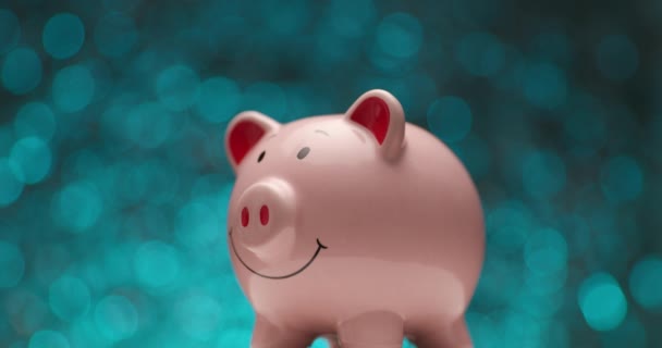 ピンクの貯金箱が青色の背景を背景に回転しながら泡が落ちていく — ストック動画