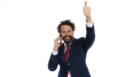 Yakışıklı iş adamı telefonda konuşuyor ve beyaz arka plandaki kameraya benzer bir görüntü veriyor.