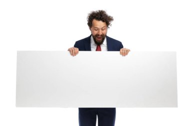 Çekici iş adamı elinde bir reklam panosu tutuyor ve aşağı bakıyor, beyaz arka planda şaşırıyor.