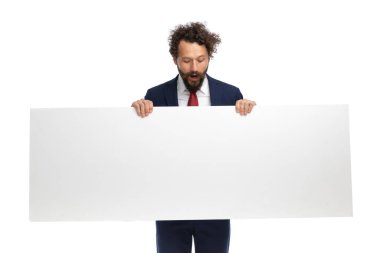 Seksi iş adamı beyaz arka planda boş bir tabela tutarken şok olmuş hissediyor
