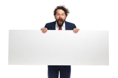 Genç işadamı beyaz arka planda boş bir tabela tutarken şok olmuş hissediyor