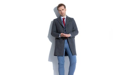 Seksi genç iş adamı avuçlarını ovalıyor, beyaz arka planda mavi takımının üzerine güzel bir ceket giyiyor.