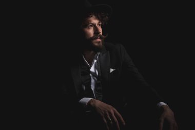 Oturmuş işadamı ellerini kucağına koyuyor ve siyah stüdyo geçmişine bakıyor.