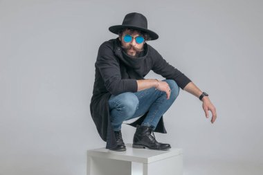 Sert tavırlı ve gri arka planda çömelmiş seksi model.