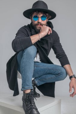 Moda adamı tavır takınıyor ve gri arka planda havalı güneş gözlüğü takıyor.