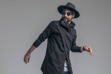 Güneş gözlüğü takan ve gri arka planda bir şapka takan seksi, sıradan bir adam.