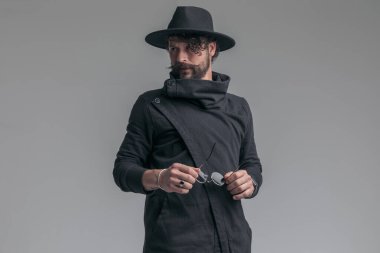 Seksi, sıradan bir adam güneş gözlüğünü çıkarıp gri arka plana yan gözle bakıyor.