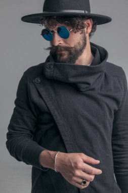 Yakışıklı, sıradan bir adam, güneş gözlüğü takıyor ve gri arka planda şapka takıyor.