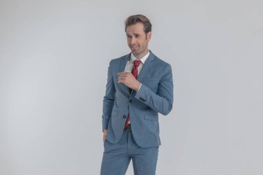 Mavi takım elbiseli mutlu bir iş adamı gülümsüyor, el ele tutuşuyor ve stüdyoda gri arka planda poz veriyor.