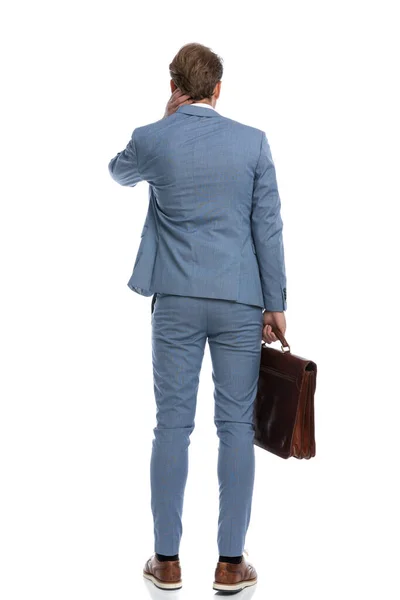青いスーツケースを着た優雅なビジネスマンが頭を掻きスタジオで白い背景に立って — ストック写真