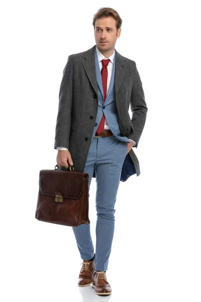年轻优雅的商人 身穿蓝色西服 手提箱手插在口袋里 边看边独立行走在工作室的白色背景下 — 图库照片