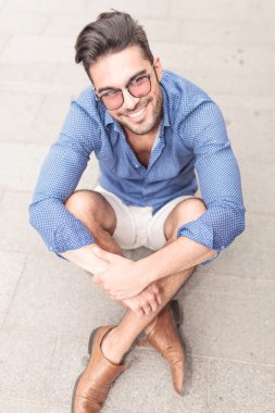 gülümseyen genç casual adam kaldırımda oturan gözlüklü
