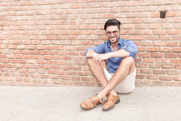 Hombre sentado cerca de la pared de ladrillo y sonrisas — Foto de Stock