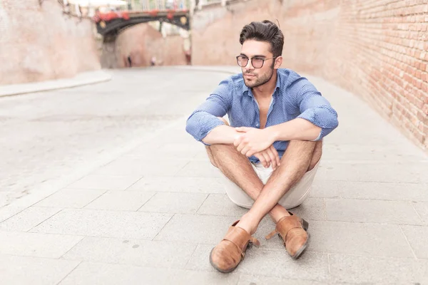 Man looks away while sitting on the sidewalk — Stock Photo, Image