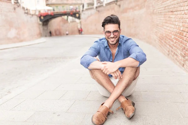 Man with glasses sitting on the sidewalk in a city — Stock Photo, Image