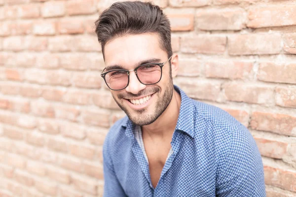 Felice uomo sorridente con gli occhiali appoggiati al muro di mattoni — Foto Stock