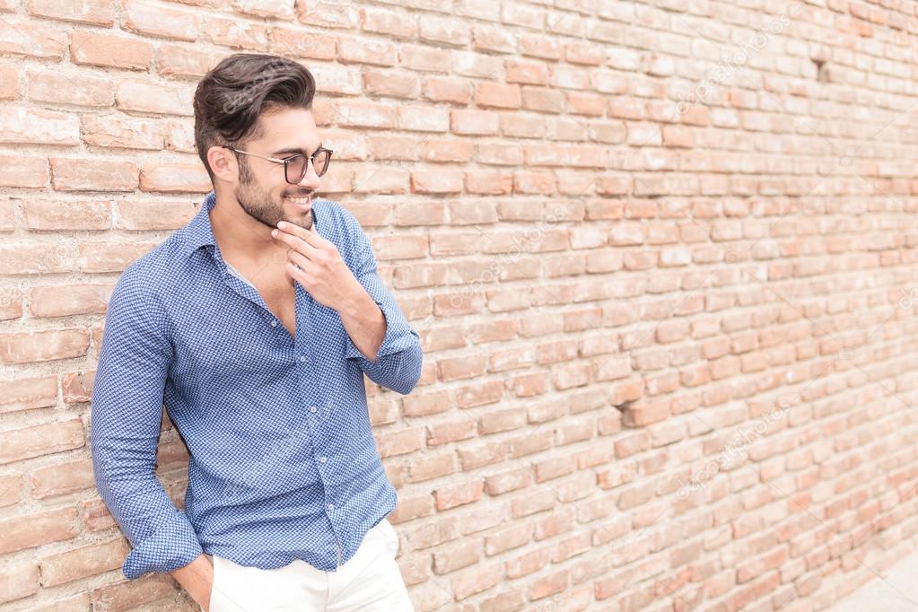 smiling casual man near brick wall wondering about something