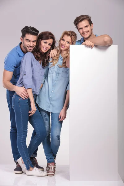 Four casual young people with a big blank billboard — Stock Photo, Image