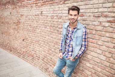 Genç casual adam güleryüzlü, bir tuğla duvara yaslanmış 